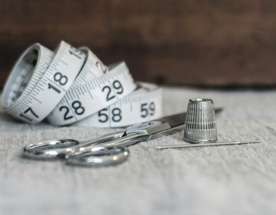 Mètre ruban, ciseaux et dé à coudre posés sur un plan de travail de tailleur